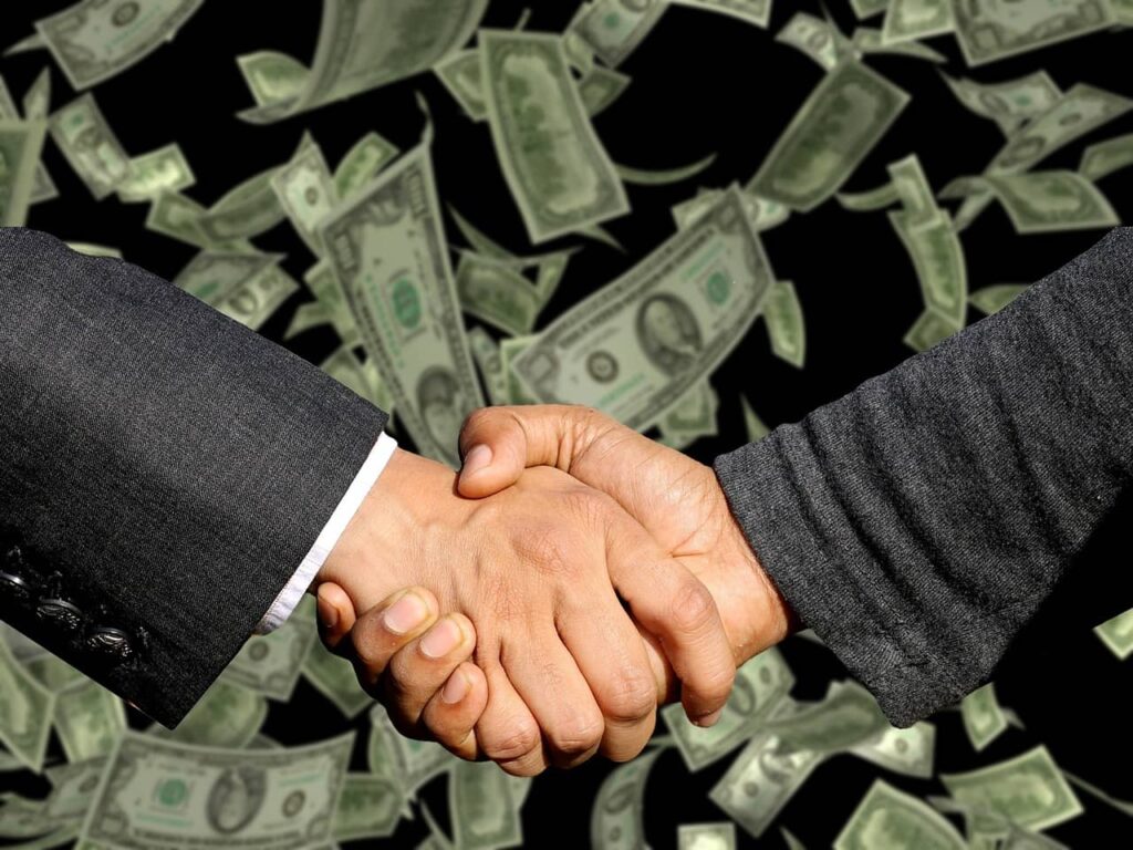 two businessmen shaking hands with a backdrop of a pile of bills