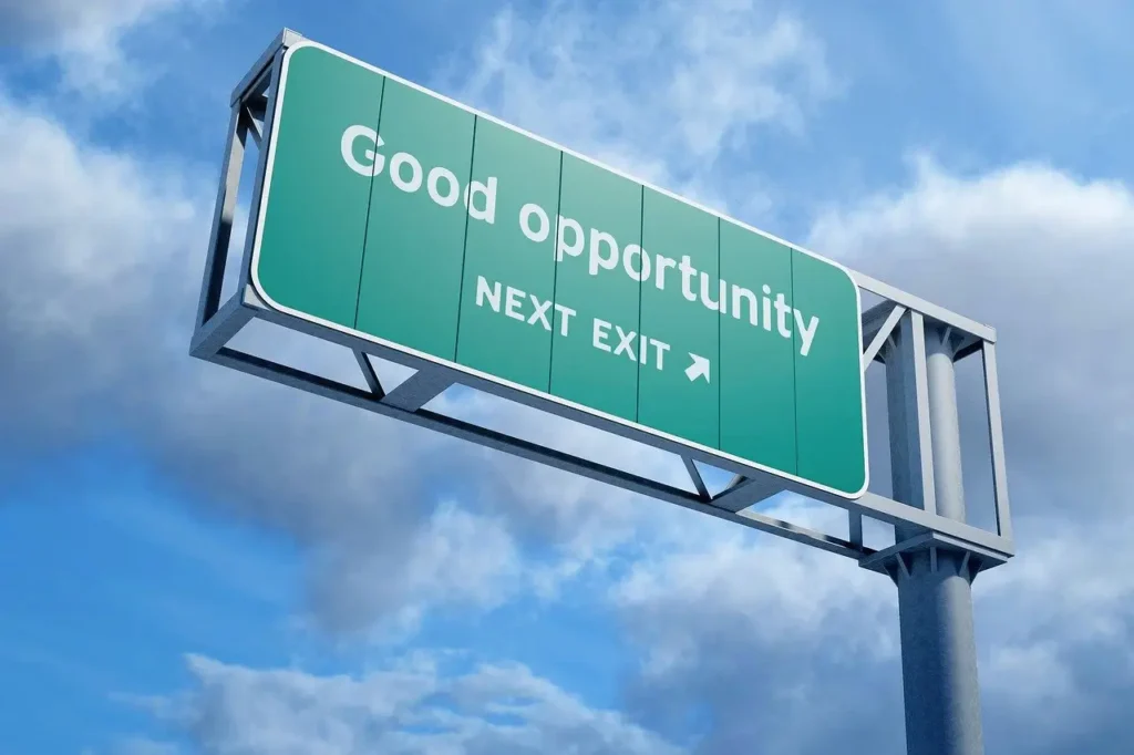 A green highway sign with the words “Good opportunity, next exit” against a blue sky with clouds