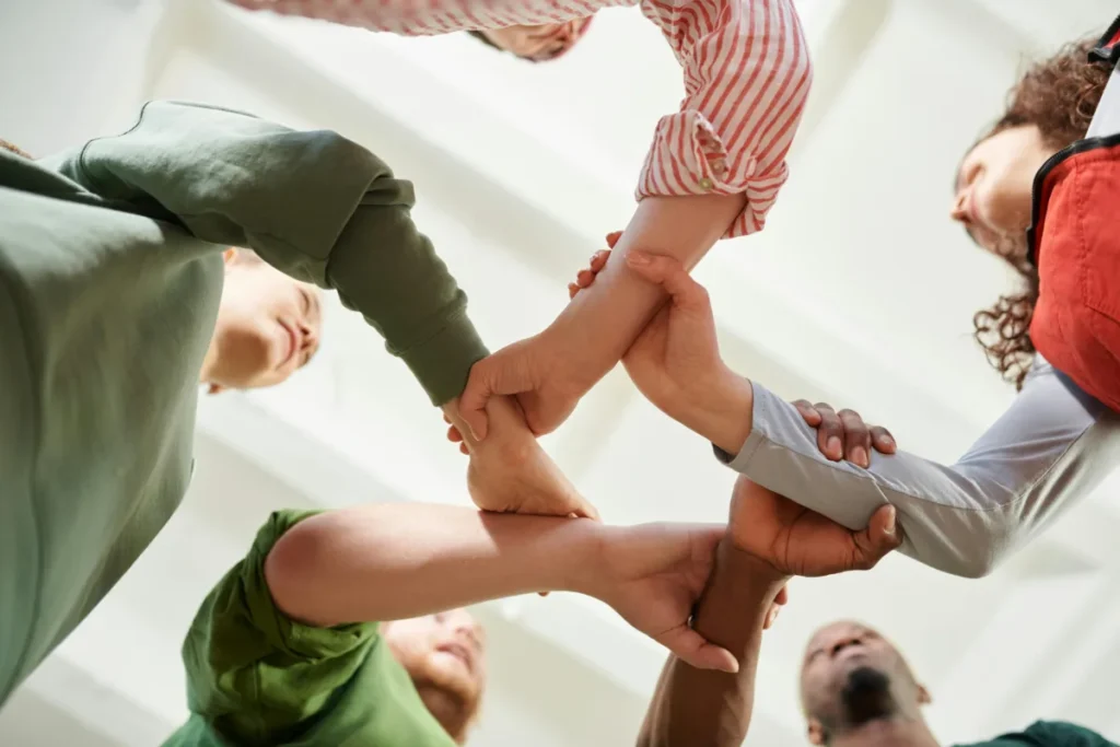 Group of people standing in a circle stacking hands together in a gesture of teamwork and unity, viewed from below
