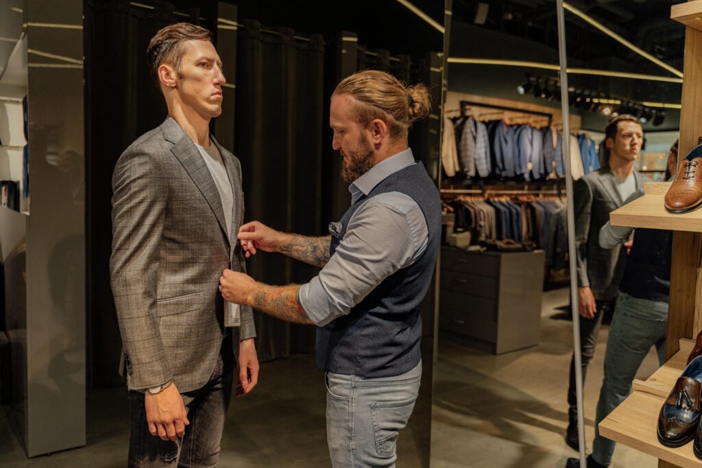 A tailor adjusts the button stance on a customer’s coat during a fitting in a menswear shop, capturing a key touchpoint in the customer journey.